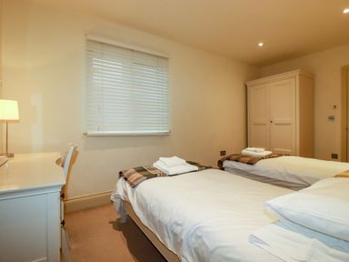 A bedroom with two single beds a desk with a lamp and chair a window with blinds and a wardrobe at Blue Horizon in Port Isaac