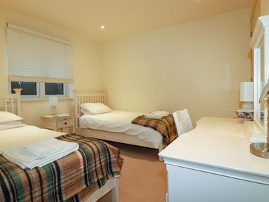A bedroom with two single beds a bedside table and a desk with a chair at Blue Horizon in Port Isaac