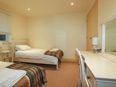 A bedroom with two single beds a desk with a chair and a mirror a bedside table with a lamp at Blue Horizon in Port Isaac