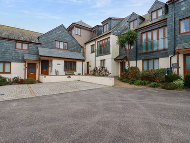 A courtyard with parked cars and attached houses with tiled roofs and large windows at Blue Horizon in Port Isaac