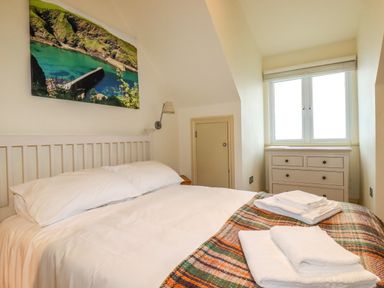 A bedroom with a white bed and folded towels on a colorful blanket a chest of drawers and a window on the right wall at Blue Horizon in Port Isaac