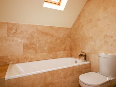 A bathroom with a white bathtub and toilet against beige tiled walls at Blue Horizon in Port Isaac