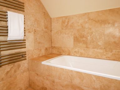 A bathroom with a white bathtub and beige tiled walls at Blue Horizon in Port Isaac