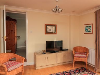A living room with a television on a cabinet two wicker chairs with cushions and framed pictures on the walls at Garden View in Hillhead near Brixham