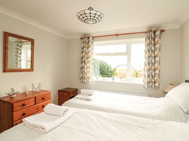 A bedroom with two single beds a wooden dresser a mirror and a window with curtains at Garden View Hillhead near Brixham
