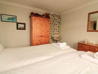 A bedroom with two single beds with white bedding wooden wardrobe and chest of drawers with a mirror at Garden View Hillhead near Brixham