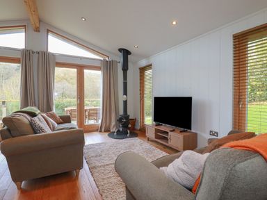 A living room with sofas a television a wood stove and large windows at 3 Hedgerows in Lanreath