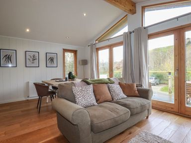 A living room with a sofa dining table chairs and large windows at 3 Hedgerows in Lanreath