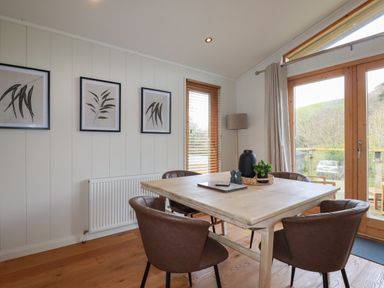 A dining area with a wooden table surrounded by four brown chairs wooden floor and framed art on the wall at 3 Hedgerows in Lanreath