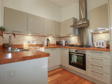 A kitchen with beige cabinets a wooden countertop a stainless steel oven and stove a microwave a toaster and a double sink at 3 Hedgerows in Lanreath