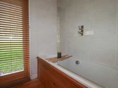 A bathroom with a bathtub wooden panel and window blinds at 3 Hedgerows in Lanreath