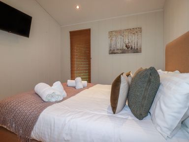 A bedroom with a bed with folded towels cushions and a wall-mounted tv at 3 Hedgerows in Lanreath