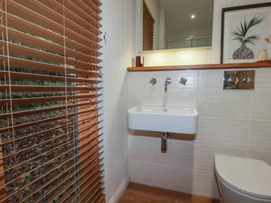 A bathroom with a wall-mounted sink wooden blinds and a framed picture at 3 Hedgerows in Lanreath