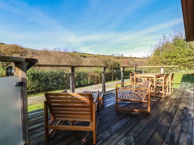 A wooden deck with outdoor wooden chairs and a table overlooking a rural landscape at 3 Hedgerows in Lanreath