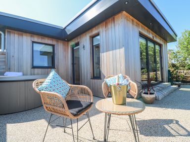 An outdoor patio with two wicker chairs a round table with a champagne bucket and a wooden house exterior at Little Victory in Pendeen