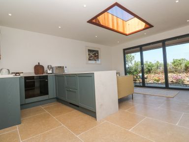 A kitchen with blue cabinets a built in oven and microwave and large windows with view of garden at Little Victory in Pendeen