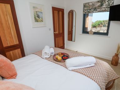 A bedroom with a bed topped with towels and a tray of food a wall mirror two wooden doors and a window with a floral blind at Little Victory in Pendeen