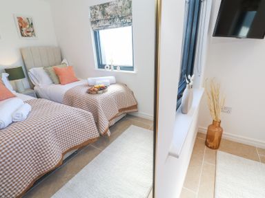 A bedroom with two single beds with checkered bedspreads and a TV on the wall at Little Victory in Pendeen