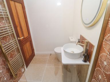 A bathroom with a wooden door a toilet a round sink with a faucet a mirror and a towel rack at Little Victory in Pendeen