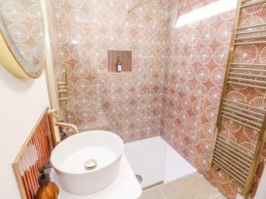 A bathroom with a vessel sink a round mirror a shower area with patterned tiles and a heated towel rail at Little Victory in Pendeen
