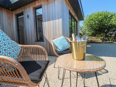 An outdoor patio with two wicker chairs with cushions and a table with a gold ice bucket and glasses at Little Victory in Pendeen