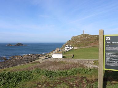 A coastal landscape with rocky shore a few white buildings and a hill with a monument at Cape Cornwall