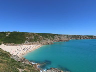 A beach with people on sand next to turquoise sea and rocky cliffs under clear blue sky at Little Victory in Pendeen