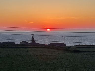 A sunset over the ocean with buildings and power lines in the foreground at Little Victory in Pendeen