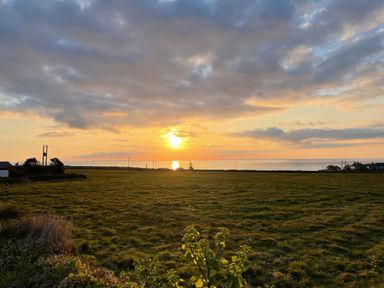 A sunset over a grassy field with scattered houses and power lines near the coast at Little Victory in Pendeen