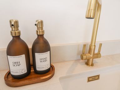 A kitchen sink area with two bottles labeled dish soap and hand wash beside a brass faucet at Little Victory in Pendeen