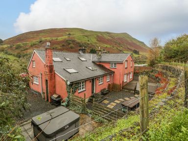A large red house with multiple chimneys and skylights surrounded by a stone wall and hillside at Ysgubor in Dinas Mawddwy near Dolgellau