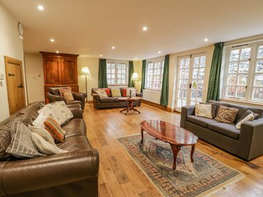 A living room with leather and fabric sofas wooden coffee tables a wooden cabinet and green curtains at Ysgubor in Dinas Mawddwy near Dolgellau