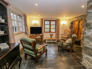 A living room with two armchairs a rocking chair a TV on a wooden stand and stone walls at Ysgubor in Dinas Mawddwy near Dolgellau