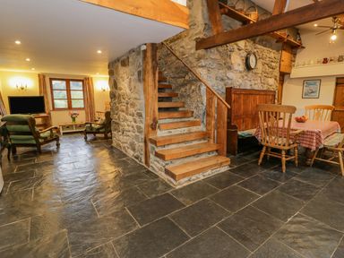 A room with a stone staircase in the center a dining table with chairs on the right and a sitting area with armchairs and a television on the left at Ysgubor in Dinas Mawddwy near Dolgellau