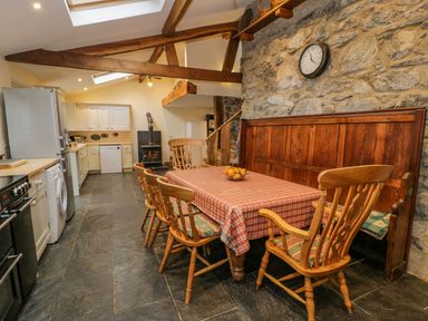 A kitchen dining area with wooden chairs a table with a checkered tablecloth and a stone wall clock at Ysgubor in Dinas Mawddwy near Dolgellau