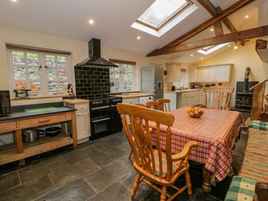 A kitchen with wooden chairs around a table with a checkered tablecloth and fruit bowl at Ysgubor in Dinas Mawddwy near Dolgellau