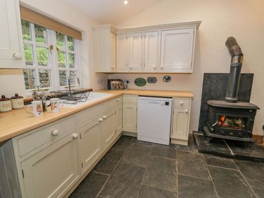 A kitchen with white cabinets a dishwasher a wood burning stove and a window at Ysgubor in Dinas Mawddwy near Dolgellau