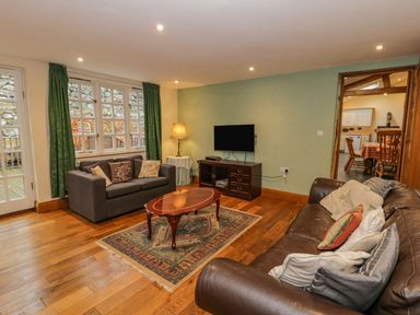 A living room with two sofas a wooden coffee table a television on a stand and large windows with green curtains at Ysgubor in Dinas Mawddwy near Dolgellau