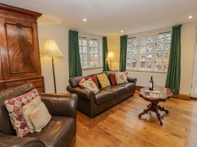 A living room with leather sofas cushions a wooden table with a wine bottle and glasses and green curtains at Ysgubor in Dinas Mawddwy near Dolgellau