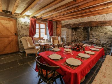A dining room with a red tablecloth set with plates and glasses next to beige armchairs and a stone wall with a fireplace at Ysgubor in Dinas Mawddwy near Dolgellau
