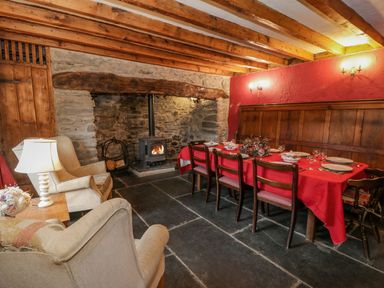 A dining room with a wooden table covered with a red tablecloth and chairs next to a stone fireplace with a wood stove at Ysgubor in Dinas Mawddwy near Dolgellau