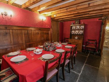 A dining room with a wooden table set with plates and glasses and a red tablecloth with a wooden cabinet with plates on display at Ysgubor in Dinas Mawddwy near Dolgellau