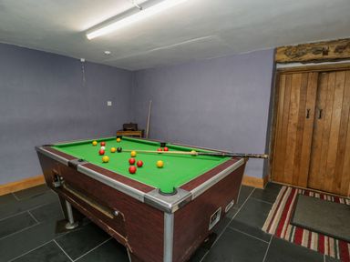 A room with a pool table with balls and cues near wooden doors and a striped rug at Ysgubor in Dinas Mawddwy near Dolgellau