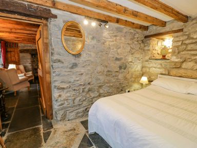 A bedroom with a bed a lamp and an oval mirror on a stone wall at Ysgubor in Dinas Mawddwy near Dolgellau