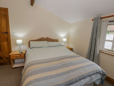 A bedroom with a double bed two bedside tables with lamps a window with patterned curtains and a wooden door at Ysgubor in Dinas Mawddwy near Dolgellau