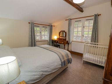 A bedroom with a double bed a crib a wooden dressing table with a chair and two windows with curtains at Ysgubor in Dinas Mawddwy near Dolgellau