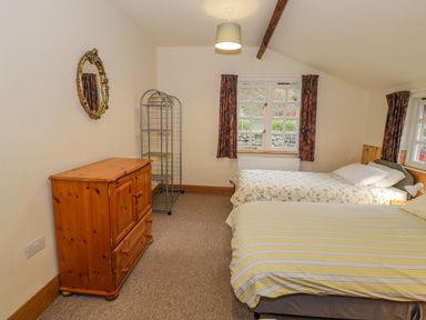 A bedroom with two single beds a wooden cabinet a metal shelving unit and floral curtains at Ysgubor in Dinas Mawddwy near Dolgellau