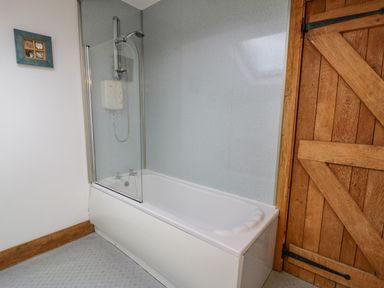 A bathroom with a bathtub and shower next to a wooden door at Ysgubor in Dinas Mawddwy near Dolgellau