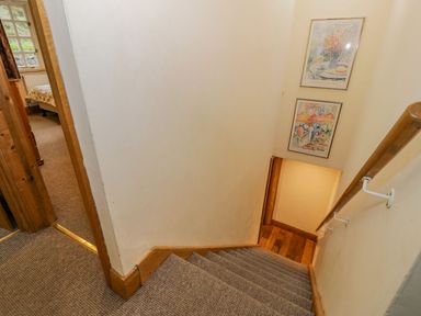 A carpeted staircase with wooden handrail and framed pictures on the wall next to a bedroom at Ysgubor in Dinas Mawddwy near Dolgellau