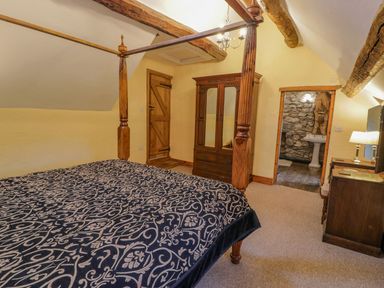A bedroom with a wooden four-poster bed a wardrobe a dresser and an adjoining bathroom at Ysgubor in Dinas Mawddwy near Dolgellau